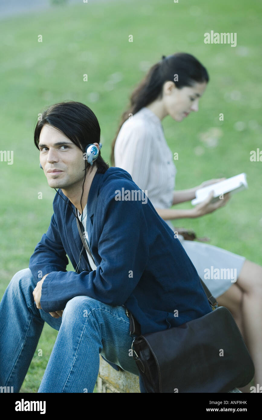 People sitting in park, man listening to headphones while woman reads book Stock Photo