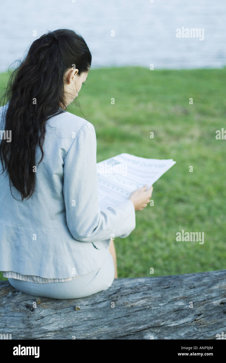 Businesswoman reading newspaper by lake, rear view Stock Photo