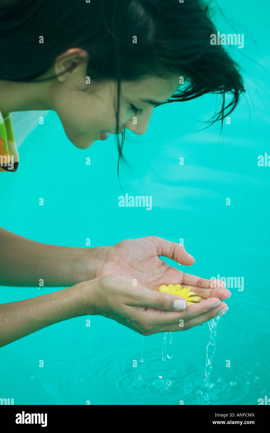 Young woman leaning over pool and holding flower in cupped hands, cropped side view Stock Photo