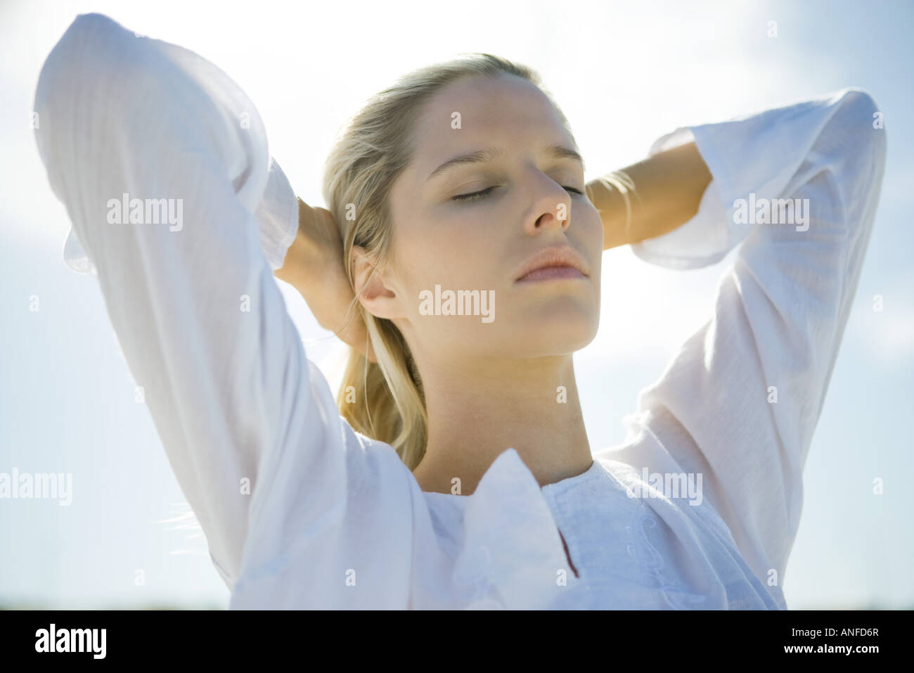 Young woman with sky in background, pushing hair back, eyes closed, low angle view Stock Photo