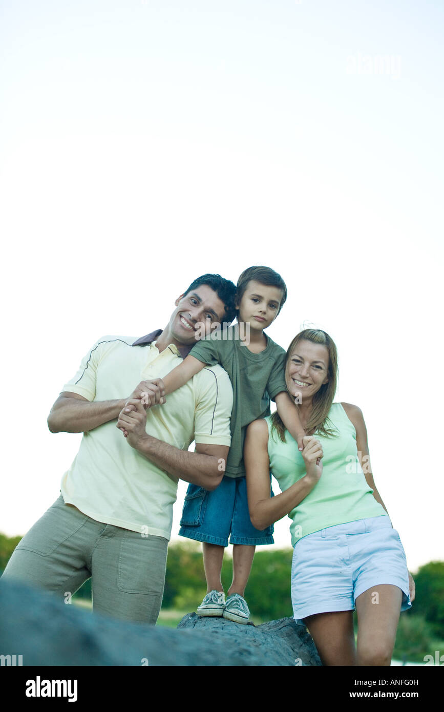 Boy standing on log, between mother and father, smiling at camera Stock Photo