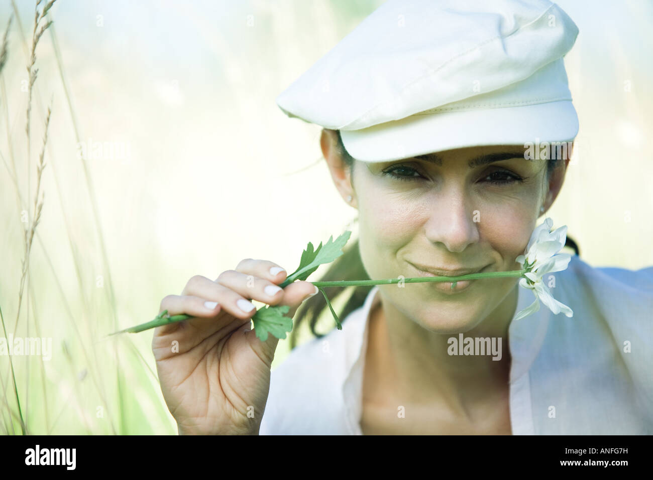 Woman in field, holding flower between lips Stock Photo
