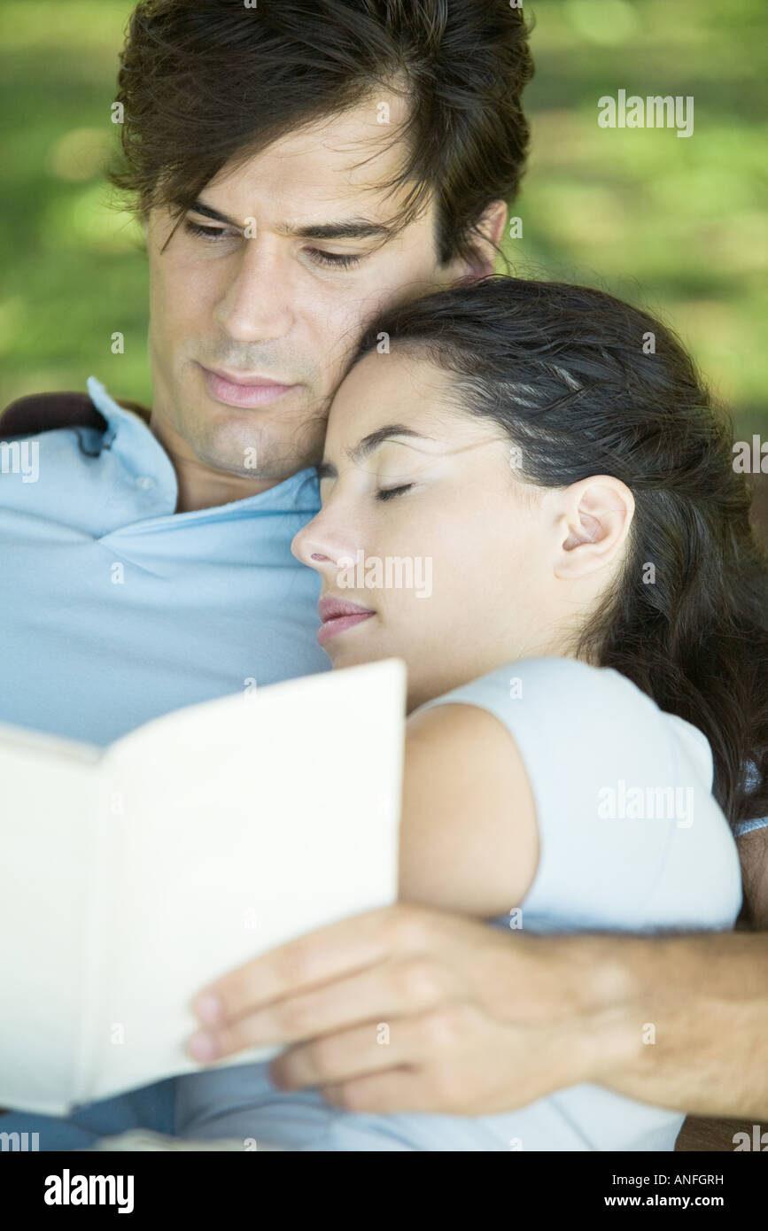 Young couple outdoors, man reading while woman sleeps with head on his shoulder Stock Photo