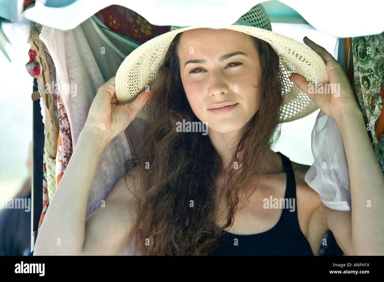 Young woman putting on straw hat, head and shoulders Stock Photo