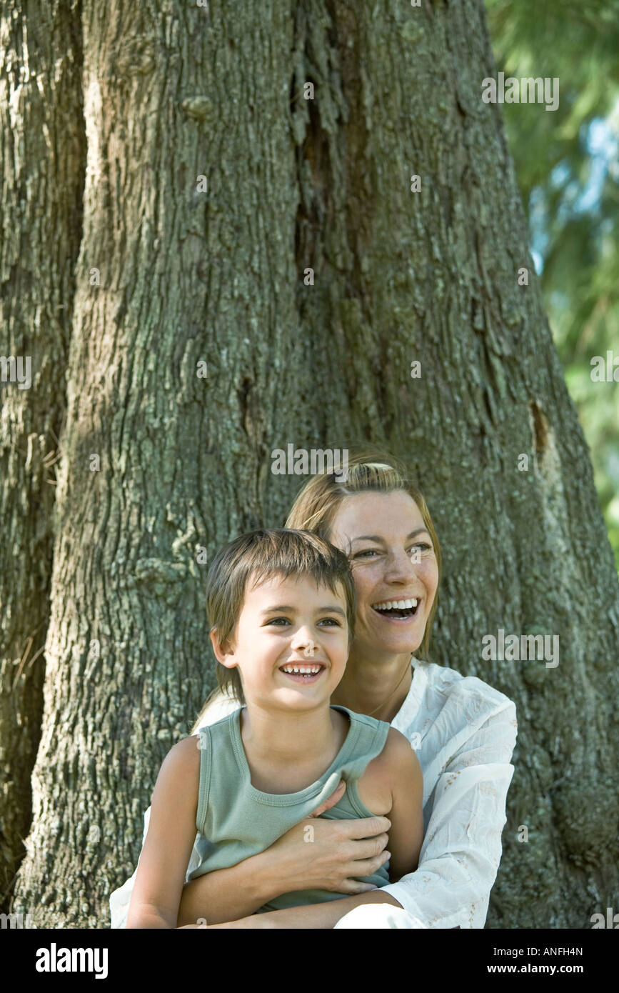 Mother and son, sitting at base of tree, laughing Stock Photo