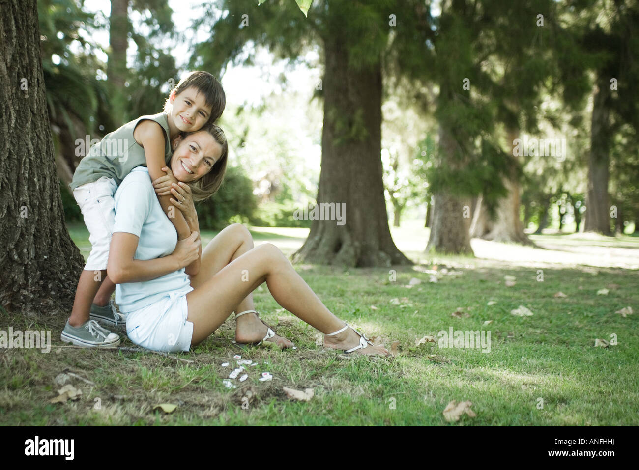 Mother and son sitting outdoors, boy hugging woman from behind Stock Photo
