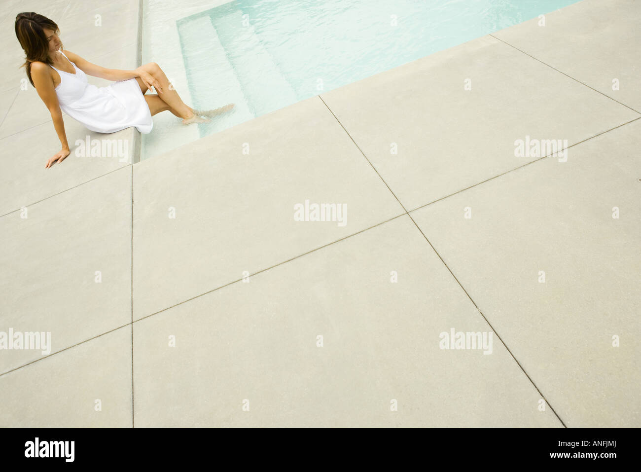 Woman sitting on edge of pool, feet in water, tilt Stock Photo - Alamy