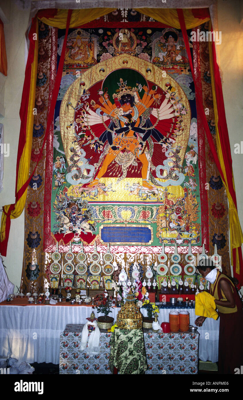 Tibetan Buddhist Kalachakra thangka painting behind a shrine with butter lamps, tended by a monk Tibetan monk. Bodh Gaya, Bihar, India Stock Photo