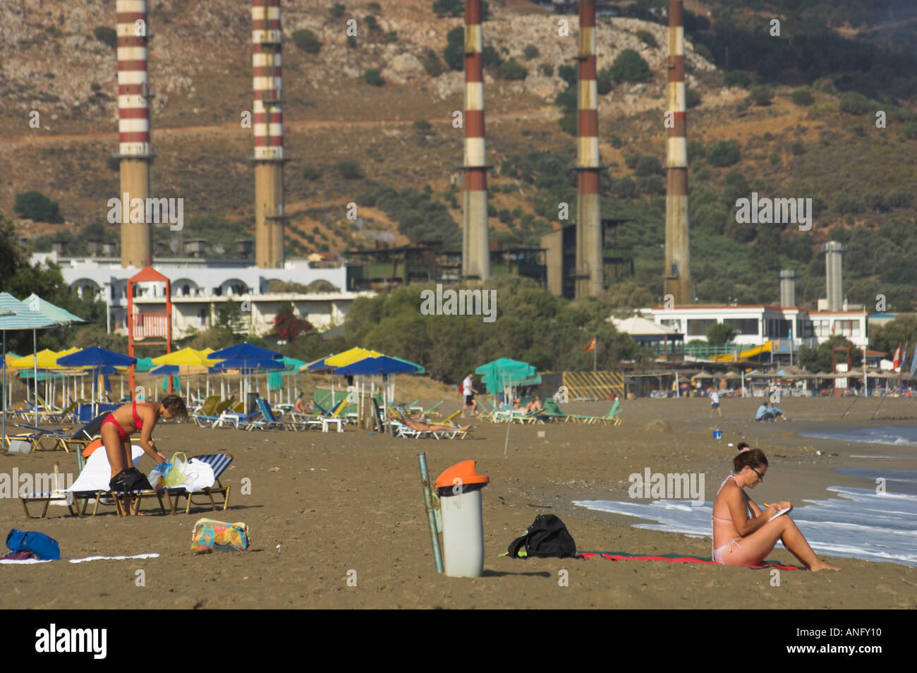 Greece Crete Ammoudara woman on the beach with umbrelas and power plant chimneys in the bkgd Stock Photo