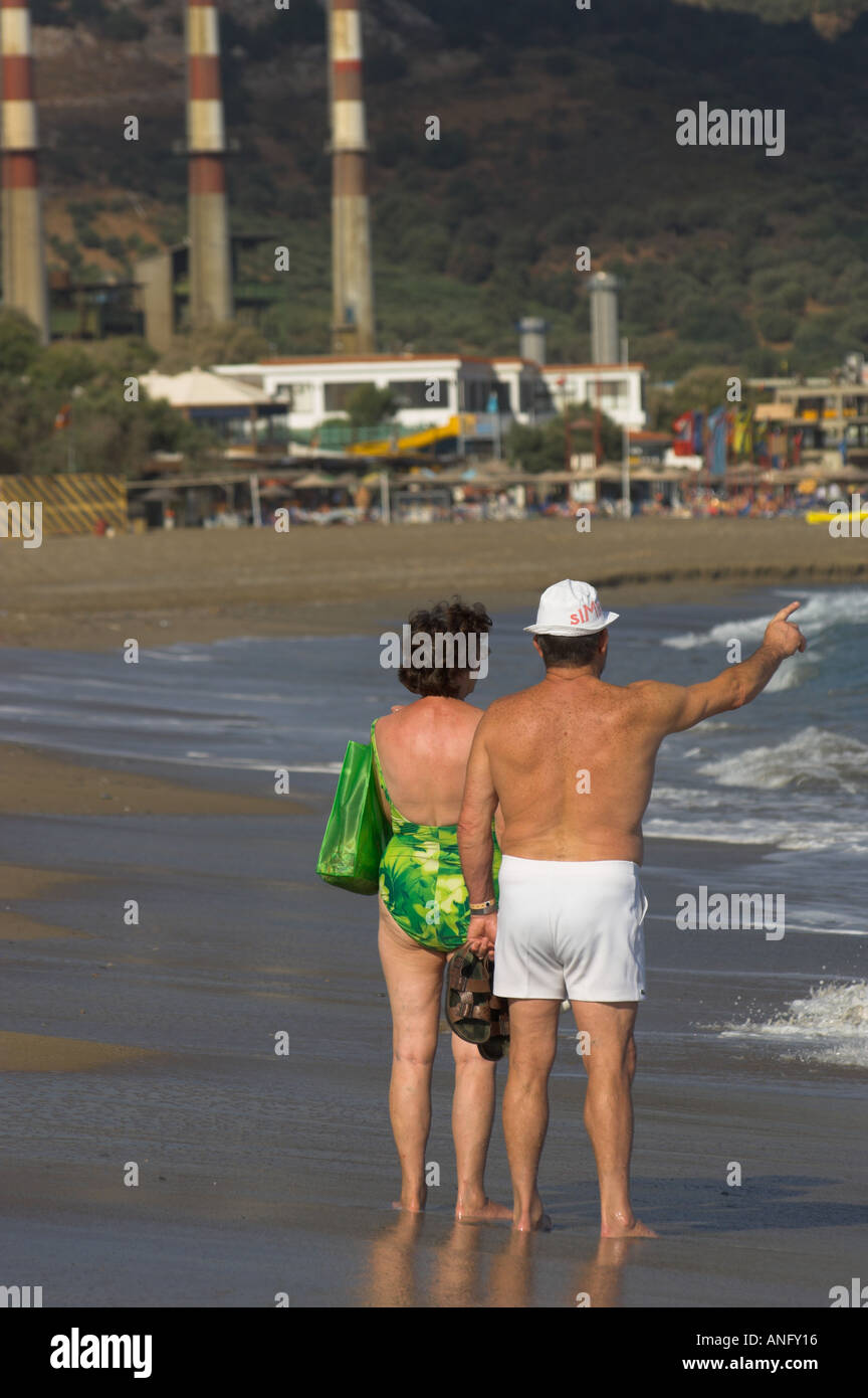 Greece Crete Ammoudara old couple standing on the beach viewed from the back with man pointing and power plant in bkgd Stock Photo