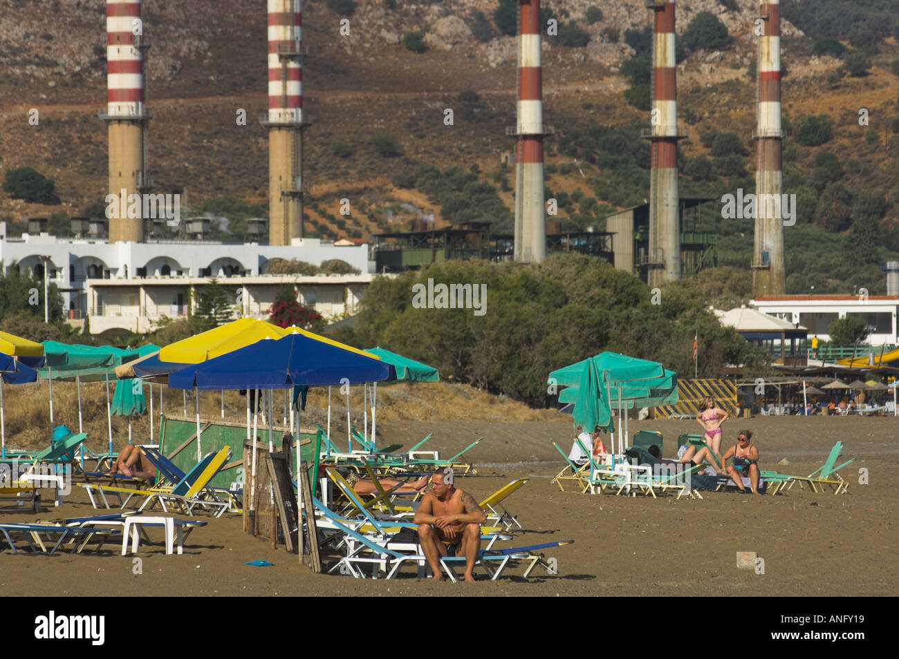 Greece Crete Ammoudara people at the beach with umbrelas and power plant chimneys in bkgd Stock Photo