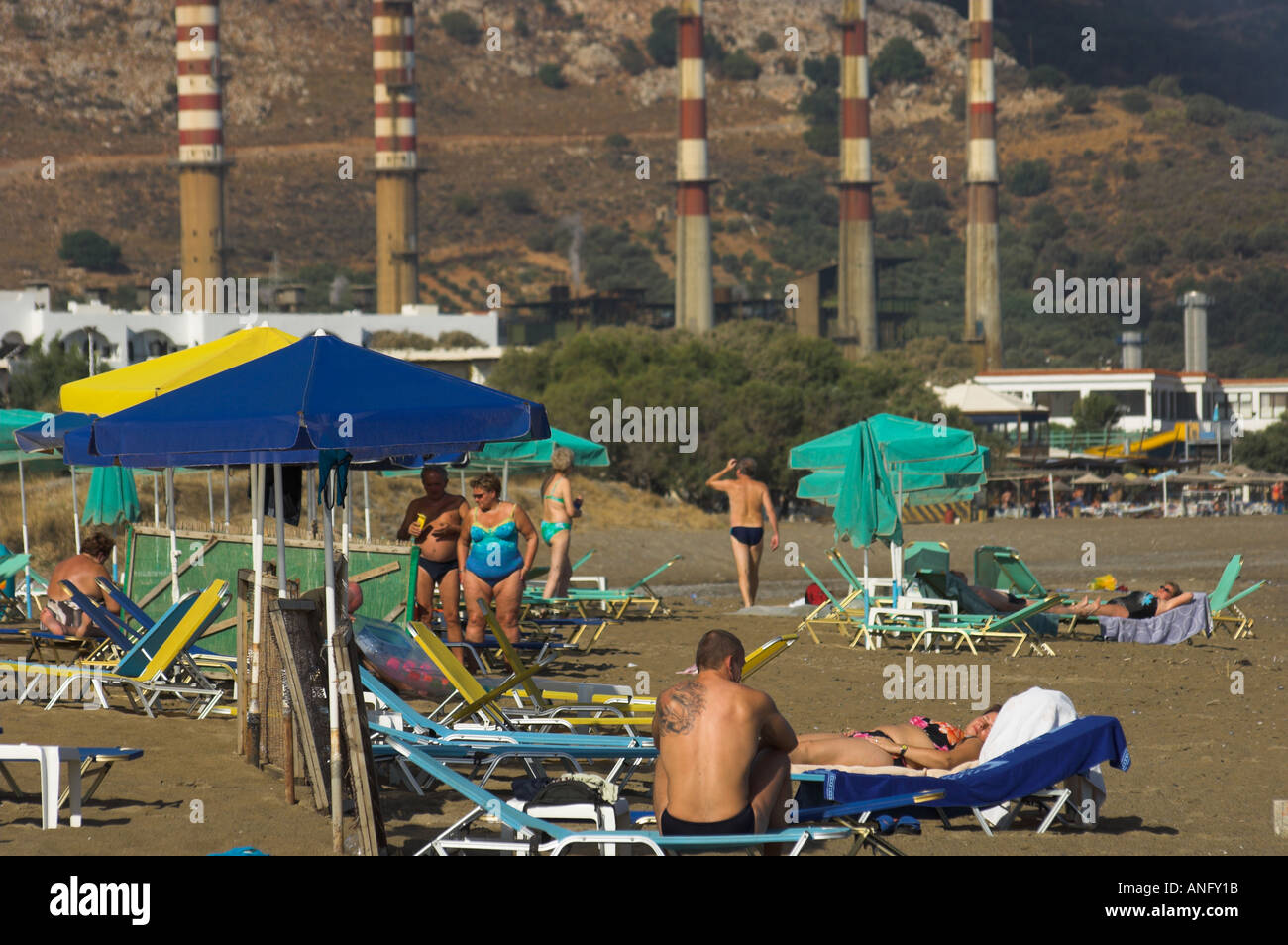 Greece Crete Ammoudara people at the beach with umbrelas and power plant chimneys in bkgd Stock Photo