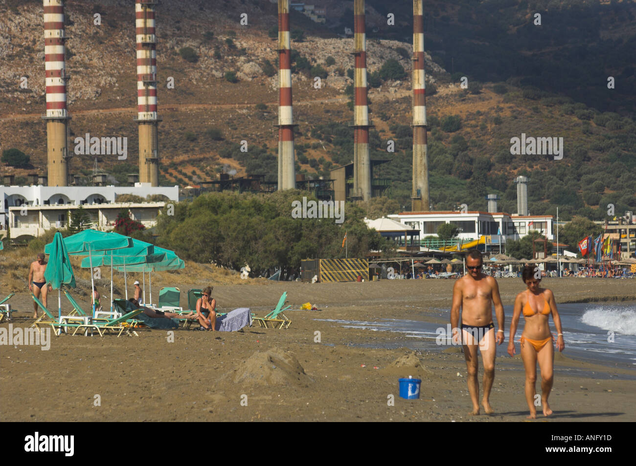 Greece Crete Ammoudara couple walking on the beach with power plant chimneys in bkgd Stock Photo