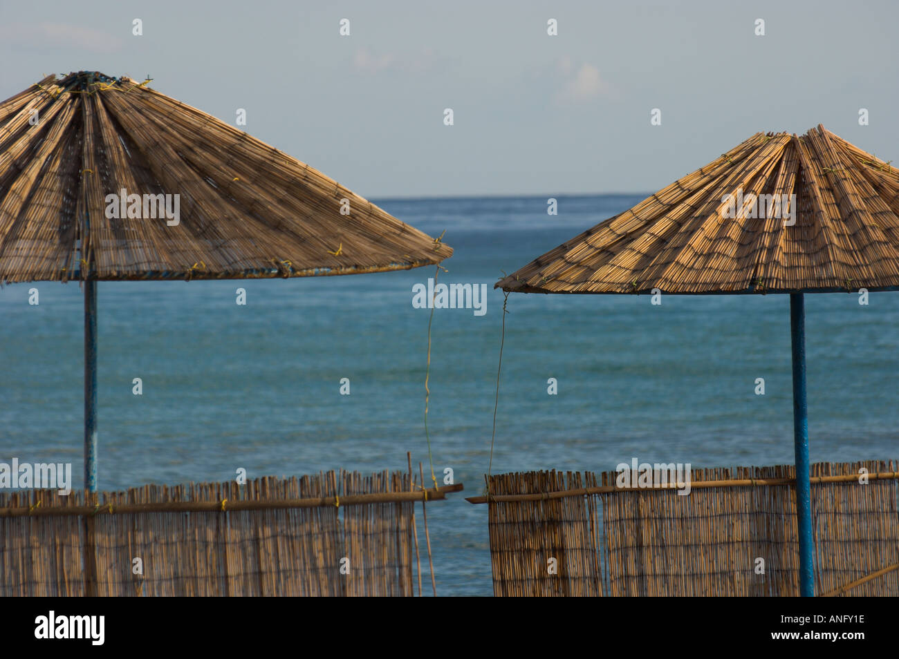 Greece Crete Ammoudara close up of 2 fine bamboo beach umbrellas and wind protection with sea in bkgd Stock Photo