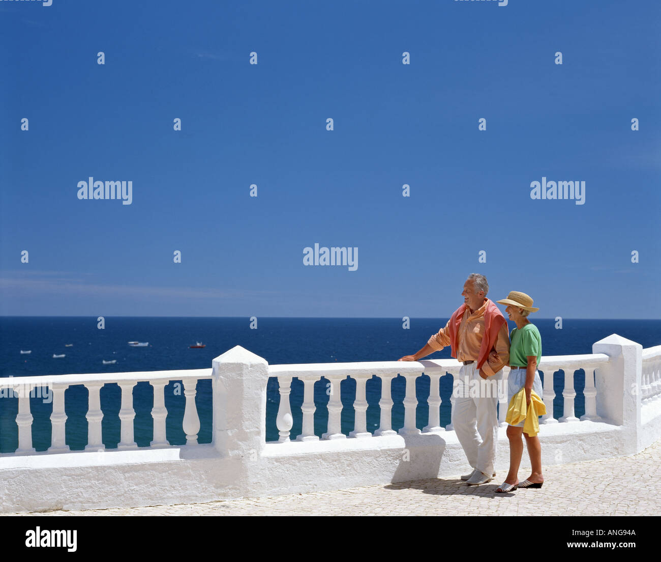 retired age couple leaning on balustrades with sea in background Stock Photo