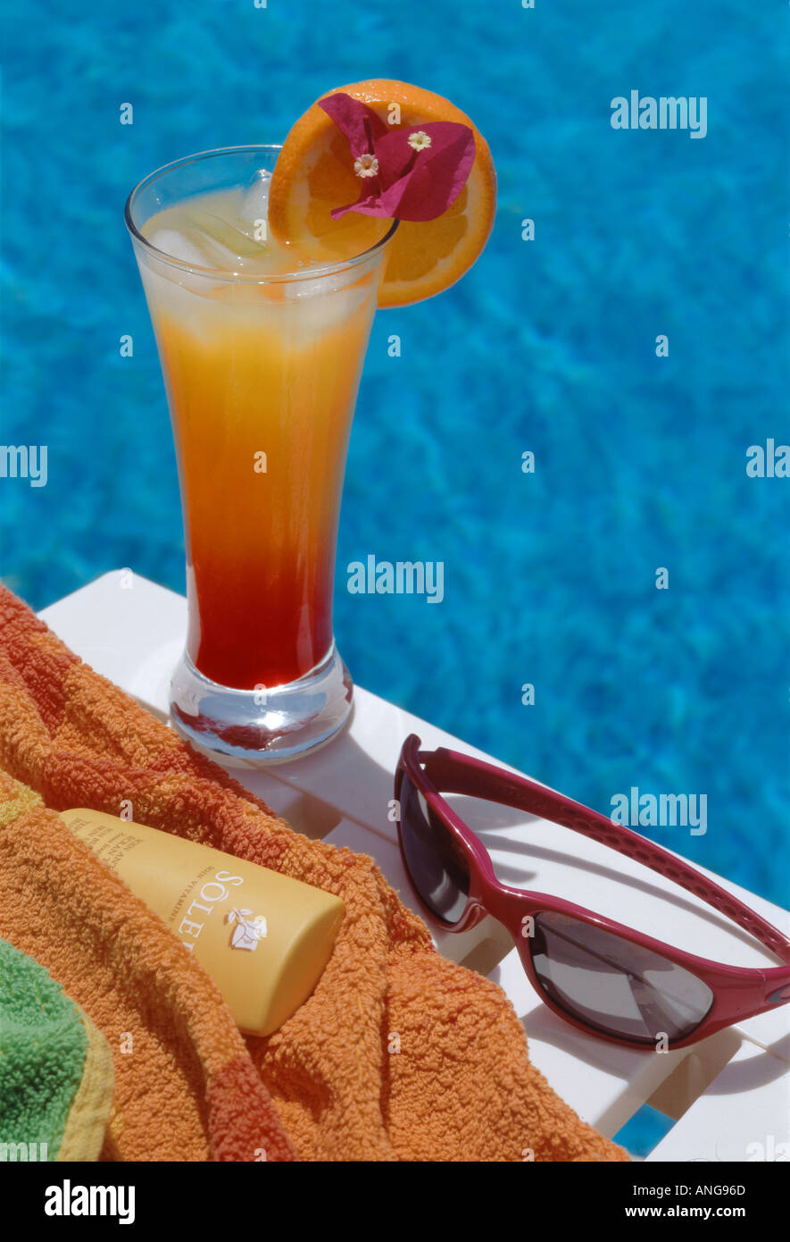 long drink sunglasses and suntan lotion on side of swimming pool Stock Photo