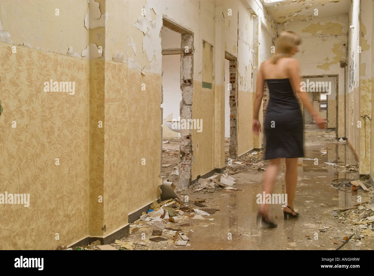 Blond woman in dress walking down hall of abandoned building Stock Photo