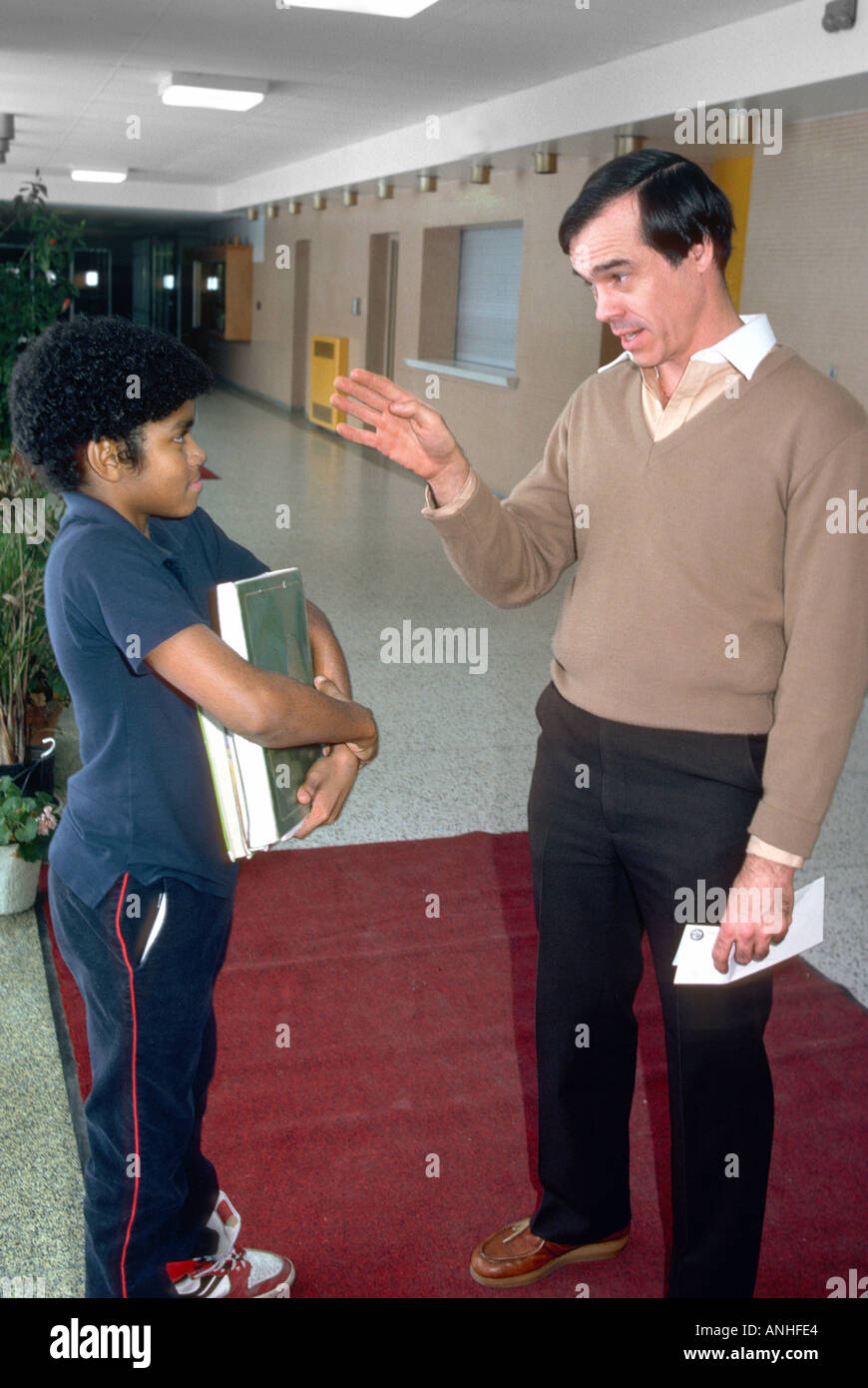 Male teacher disciplines middle school student between classes in hallway Stock Photo