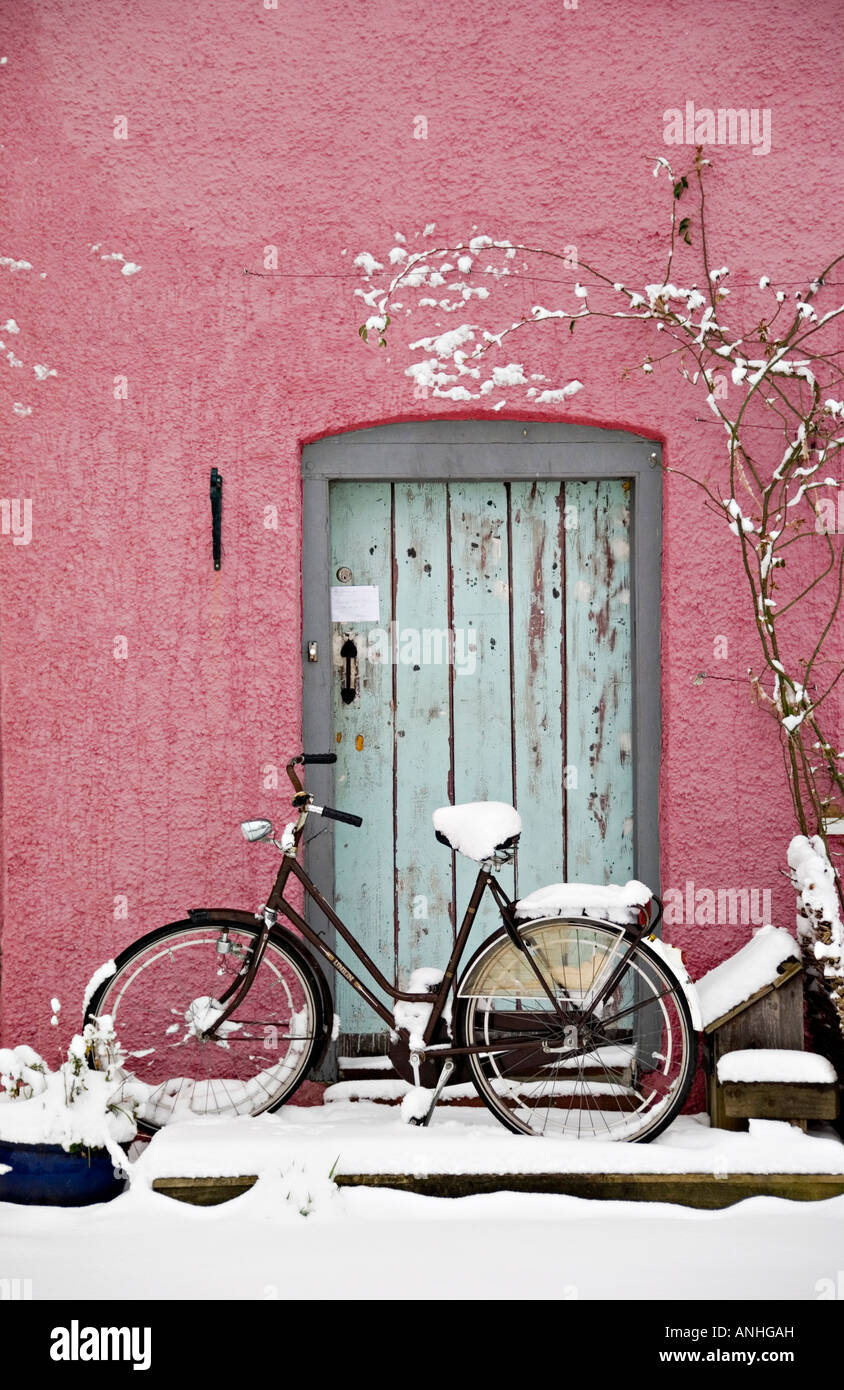 A snowy winter day in Presteigne, Powys, Wales, UK. An old bicycle leaning against a pink wall Stock Photo