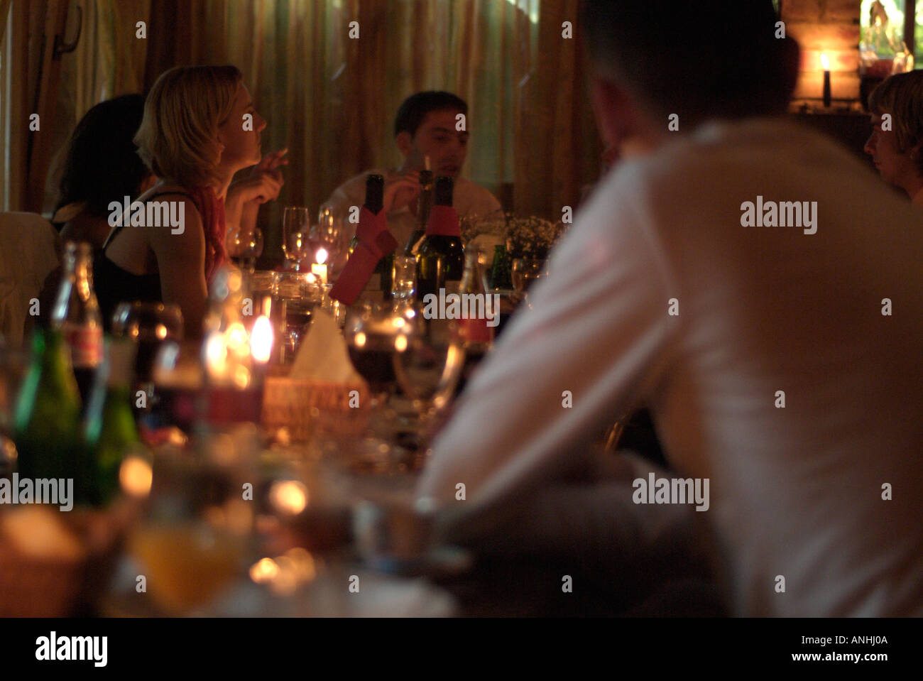 People Sitting Around a Candlelit Dining Table Enjoying Food and Drink Stock Photo