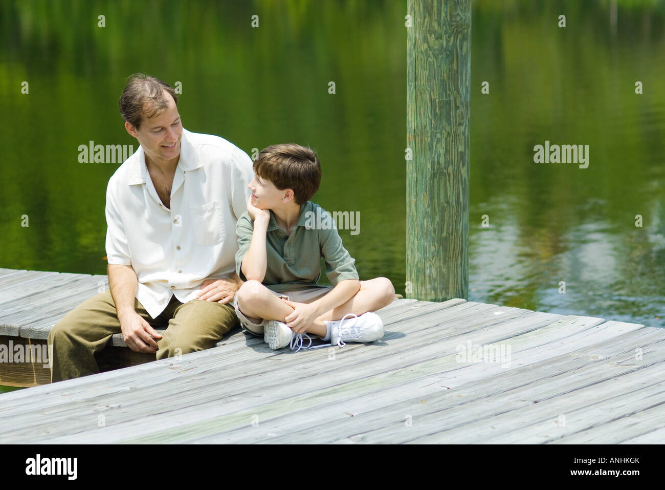 Father and son sitting on dock, smiling at each other Stock Photo - Alamy