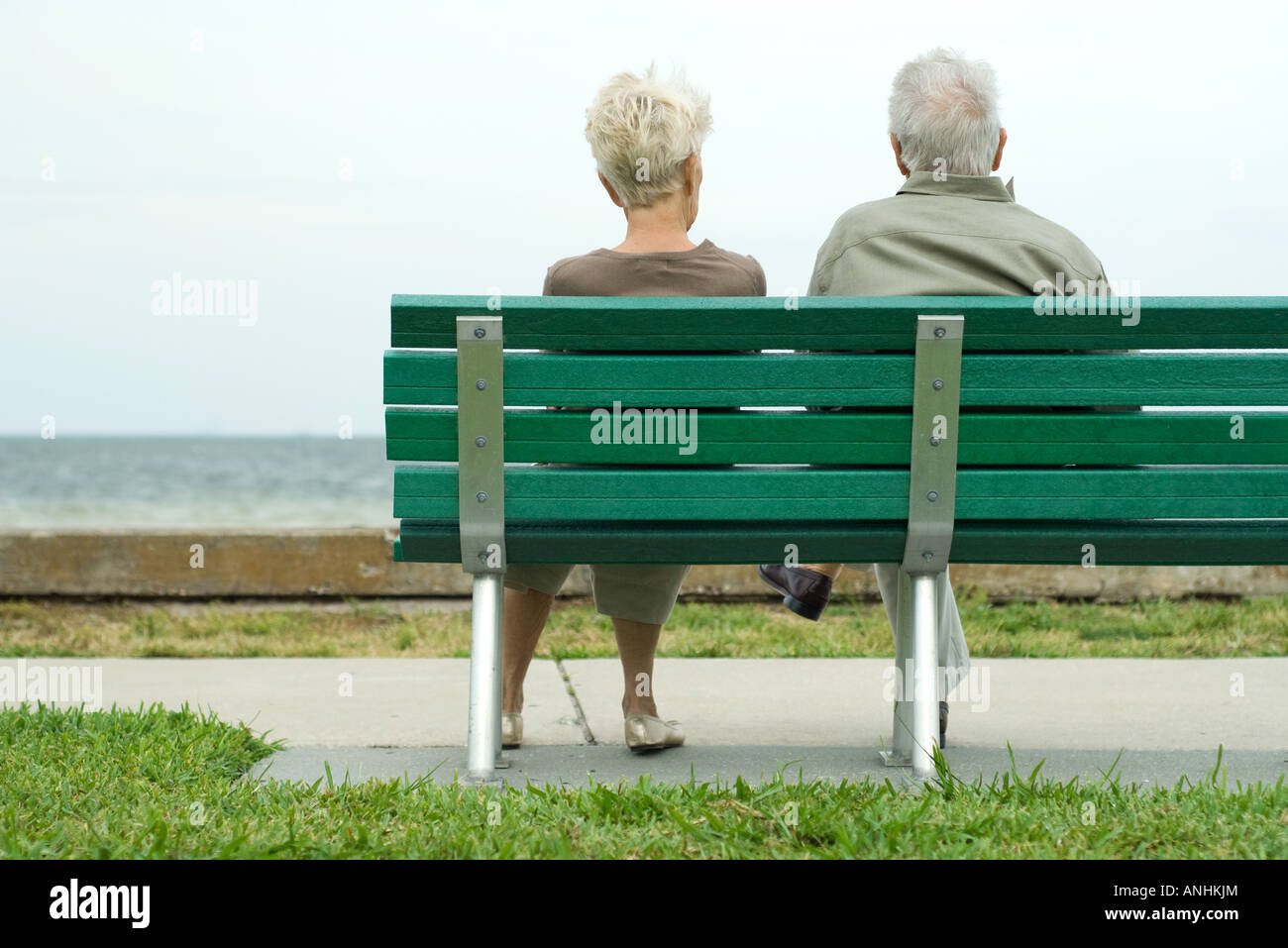 Couple sitting on bench looking at ocean, rear view Stock Photo - Alamy