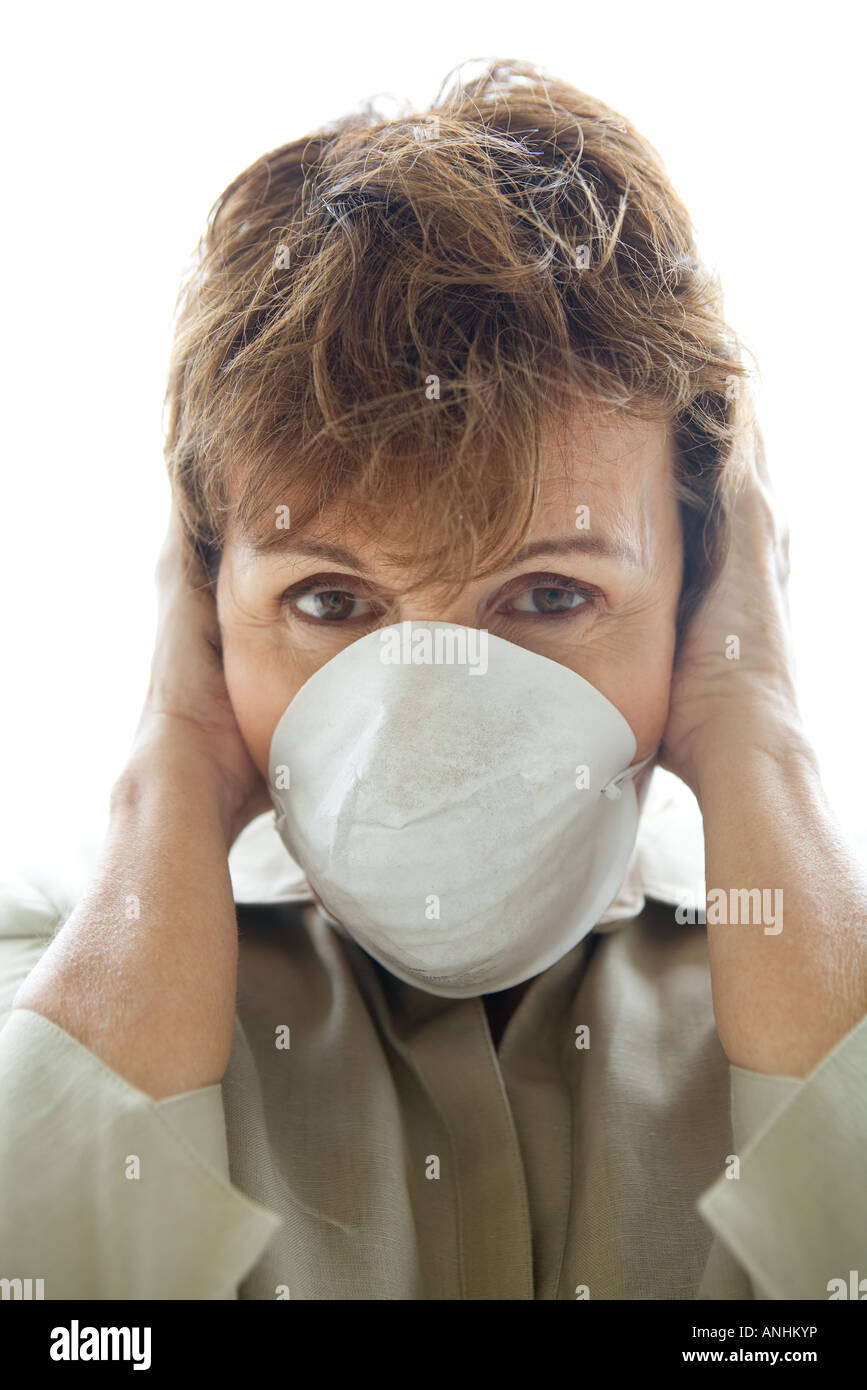 Woman with hands over ears wearing pollution mask, looking at camera Stock Photo