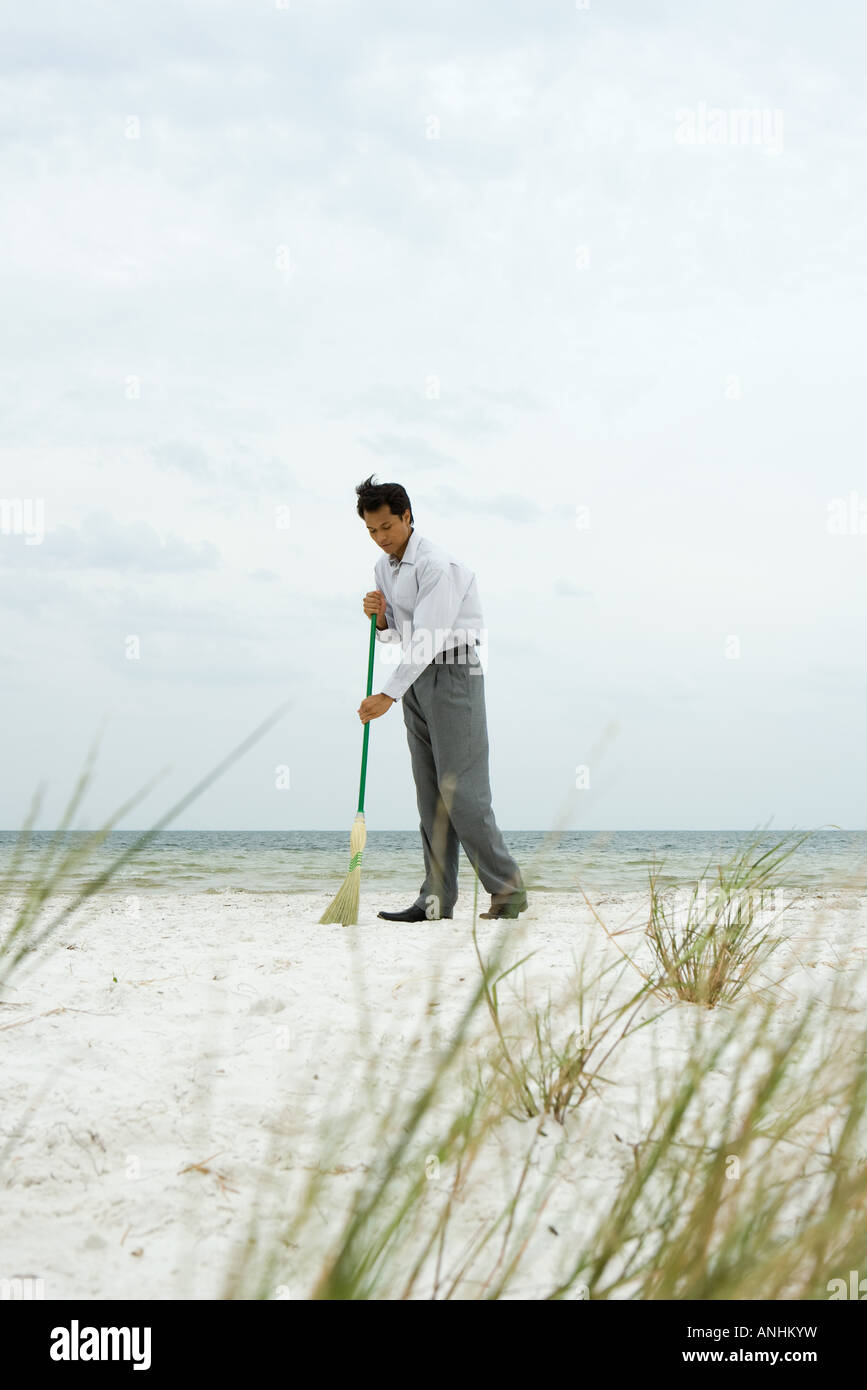 Man standing at the beach sweeping sand with broom Stock Photo Alamy