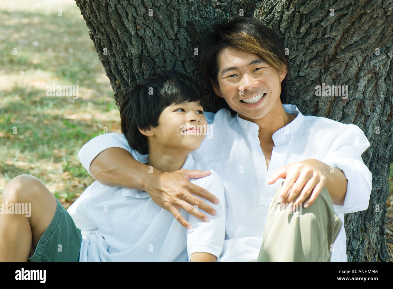 Father and son under tree together, man smiling at camera Stock Photo ...