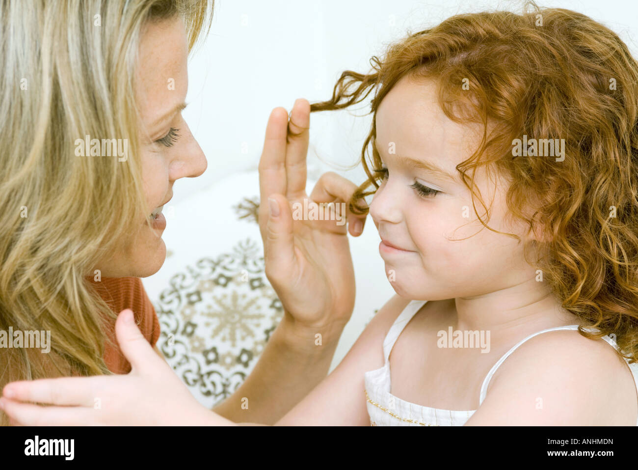 Mother and daughter touching each other's hair, both smiling Stock Photo