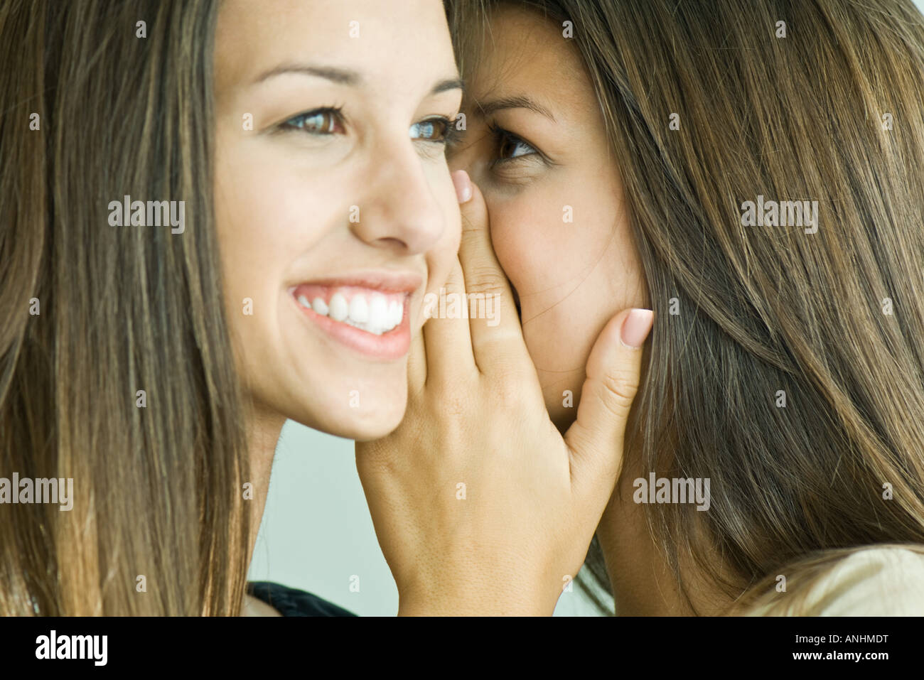 Teenage girl whispering in twin sister's ear, close-up Stock Photo