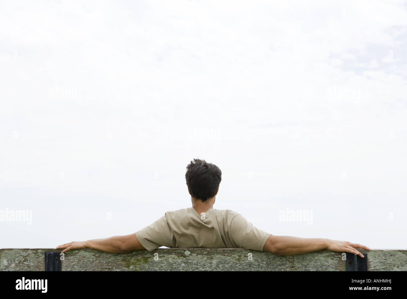 Man sitting on bench with arms outstretched, looking at sky, rear view