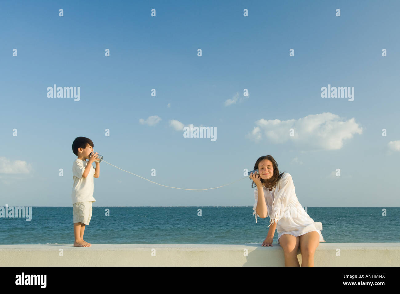 Boy speaking to woman through tin can phone, ocean horizon in background Stock Photo