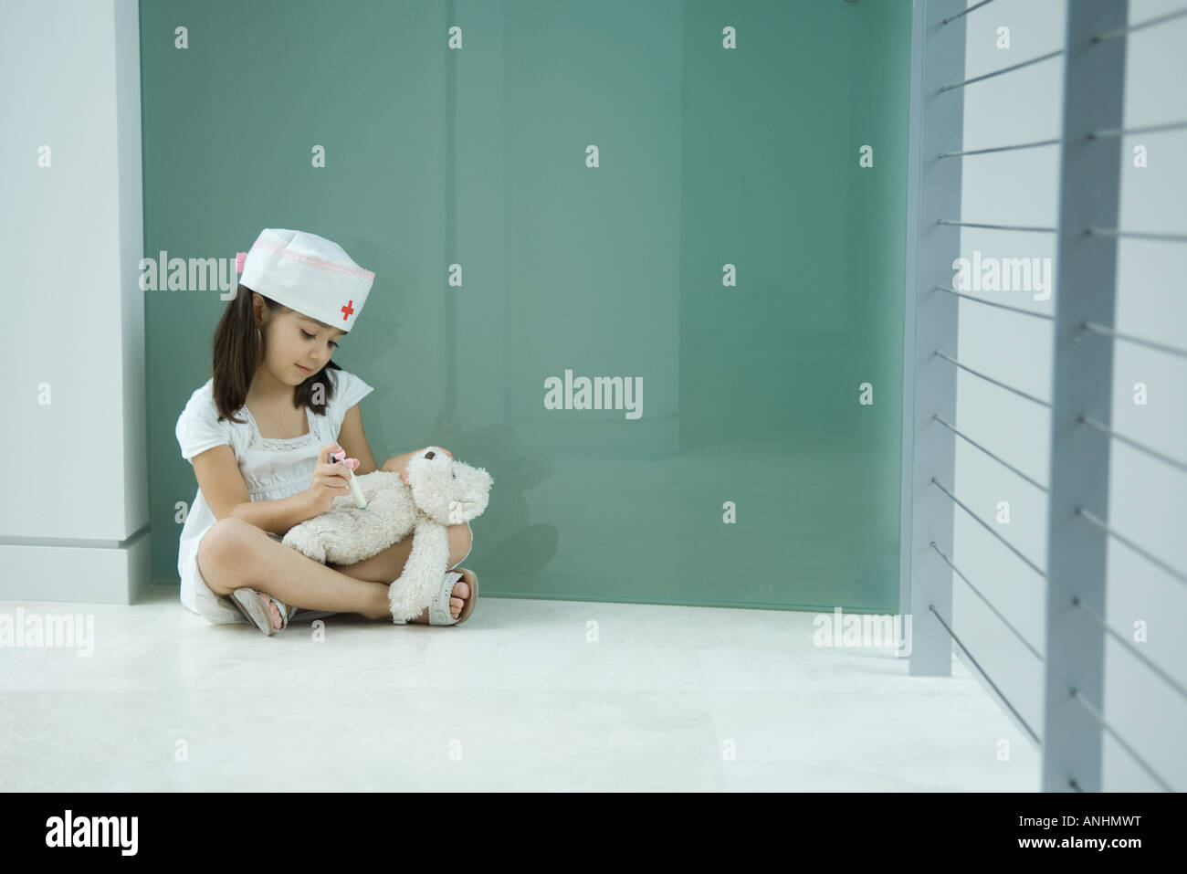 Little girl in nurse hat giving teddy bear shot Stock Photo