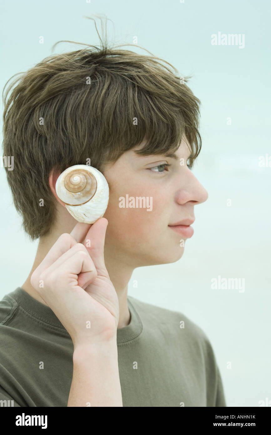 Teen boy holding up seashell to ear, profile Stock Photo - Alamy