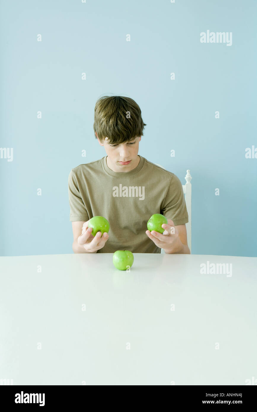 Teen boy holding up comparing three apples Stock Photo