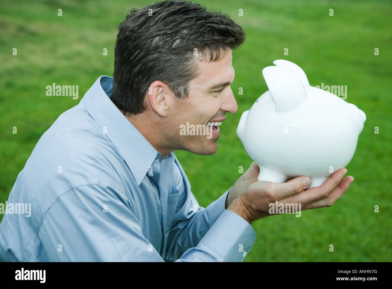 Man holding up piggy bank to face, smiling, side view Stock Photo - Alamy