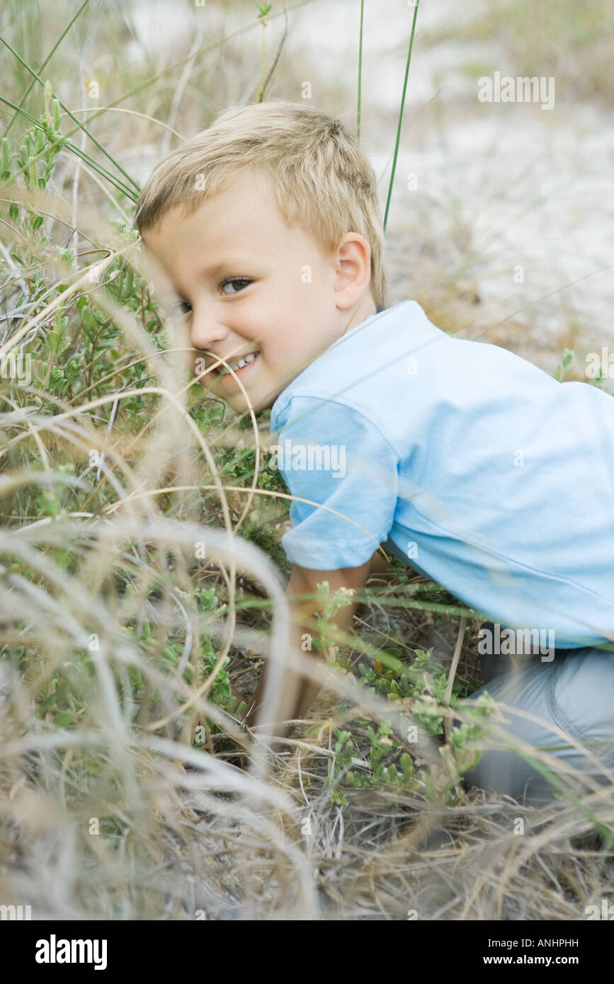 Young boy crouching in tall grass, looking over shoulder at camera Stock Photo