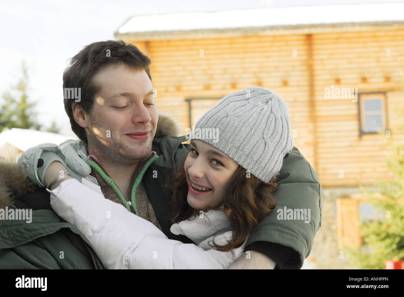 Teen girl hugging young man, looking over shoulder at camera, laughing Stock Photo