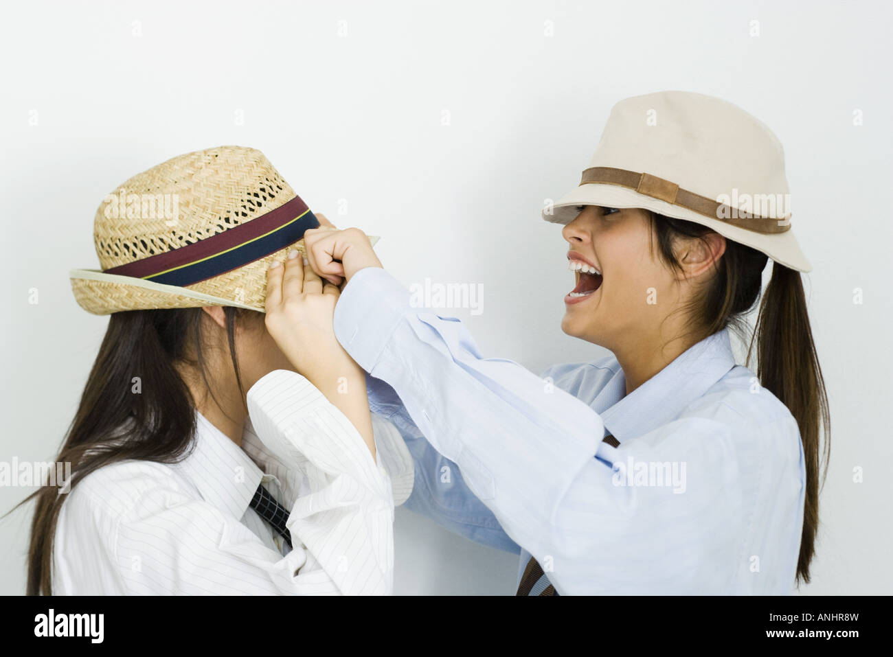 Teenage girl pulling hat over her friend's face, laughing Stock Photo