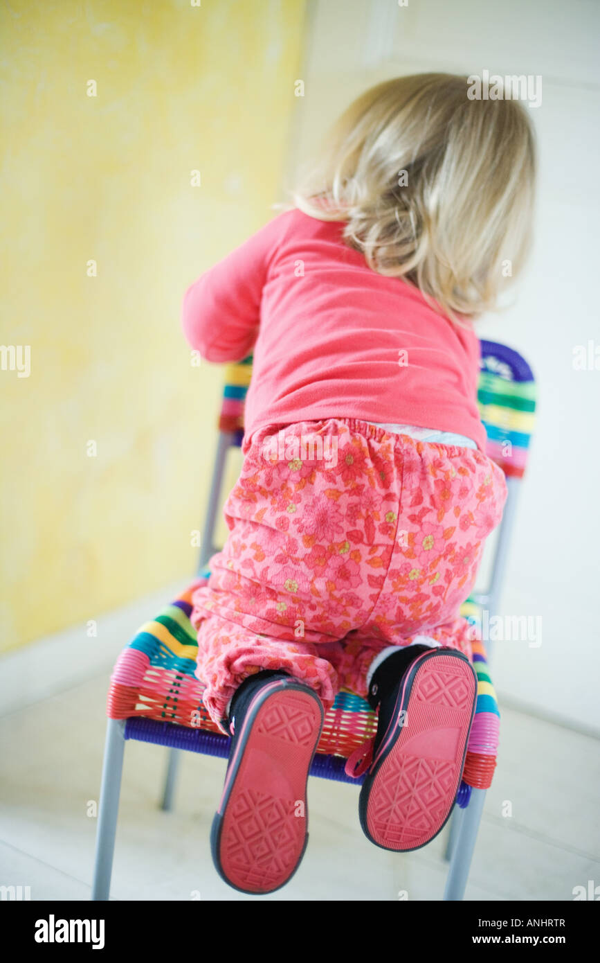 Blonde toddler girl climbing on chair, rear view Stock Photo Alamy
