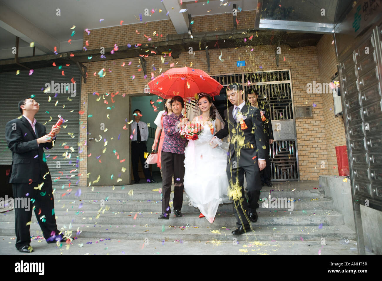 Chinese wedding, bride and groom leaving under confetti, bride covered by red parasol Stock Photo