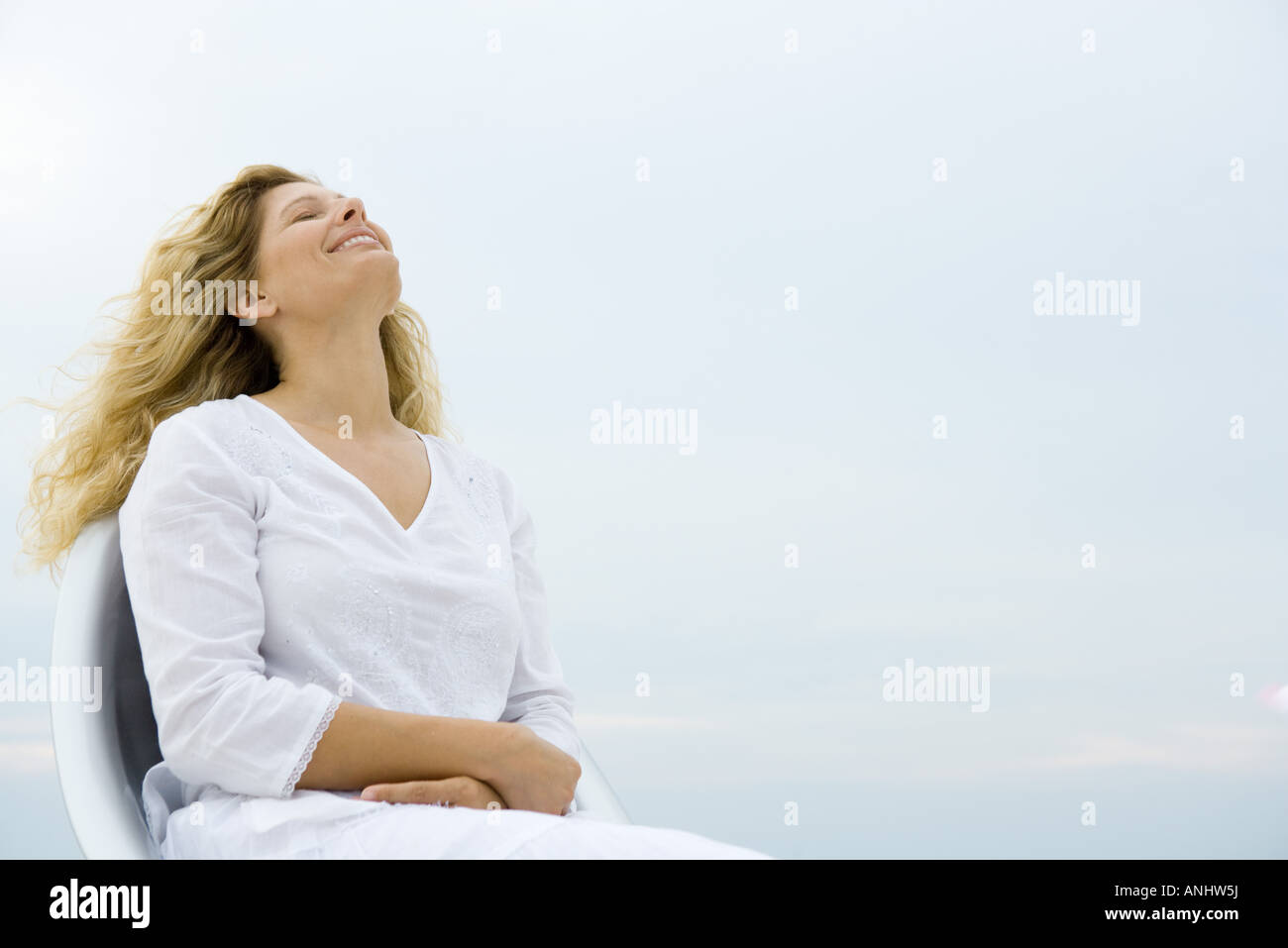 Woman sitting with eyes closed and head back, smiling, sky in background, low angle view Stock Photo