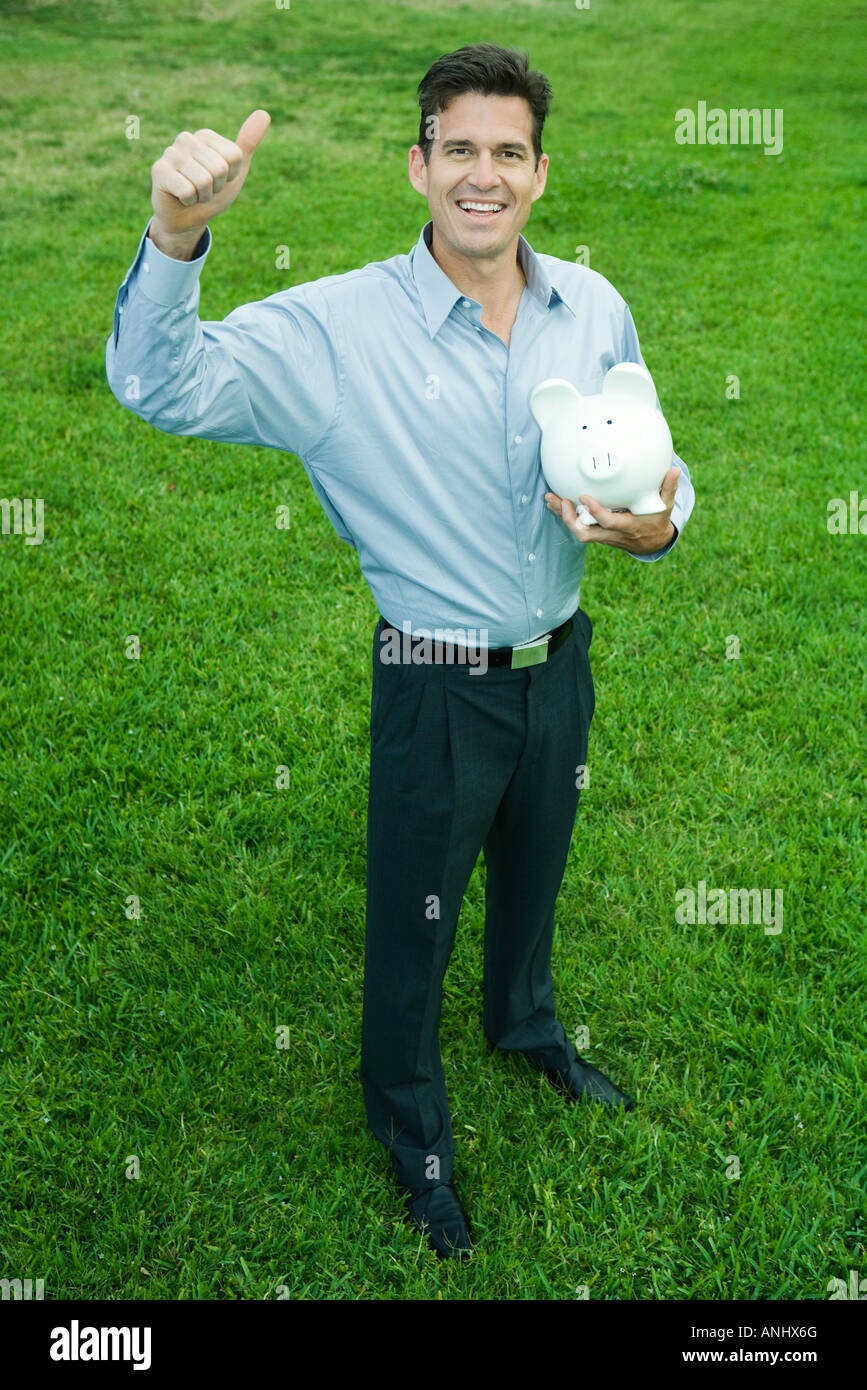 Man holding piggy bank and giving thumbs up signal while smiling at ...