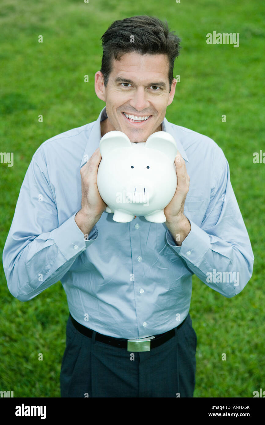Man holding piggy bank under chin, smiling at camera Stock Photo - Alamy
