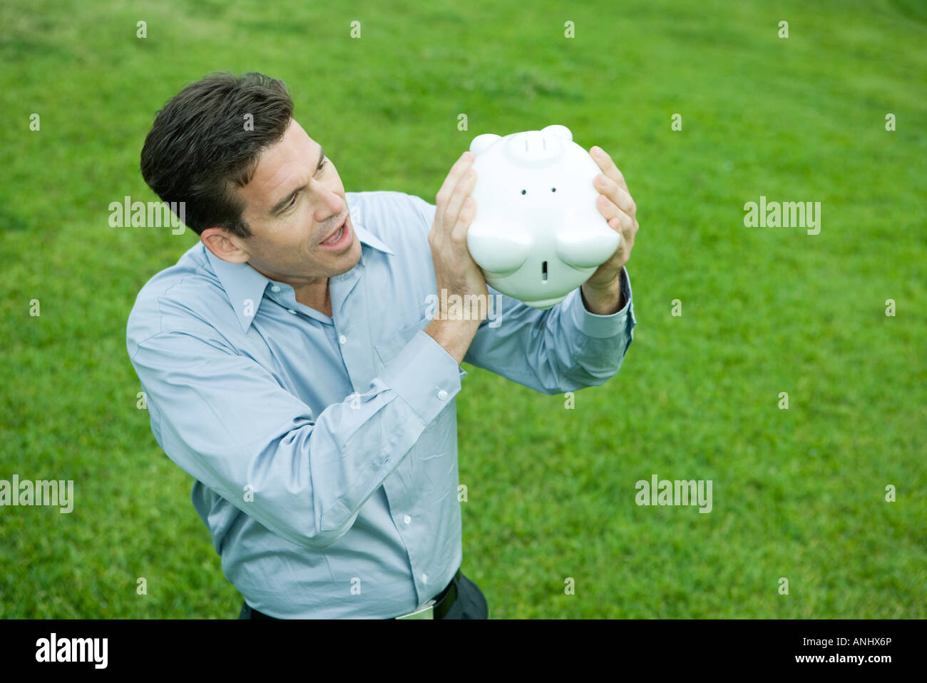 Man holding piggy bank upside down, looking surprised Stock Photo - Alamy