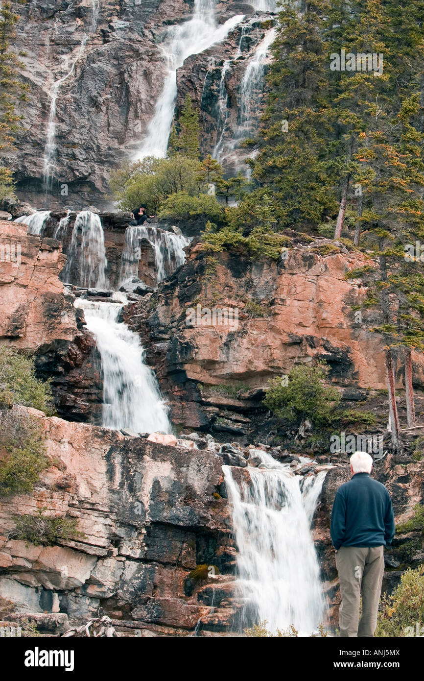 An elderly man stood on a rock looking up at a glacial waterfall Stock Photo