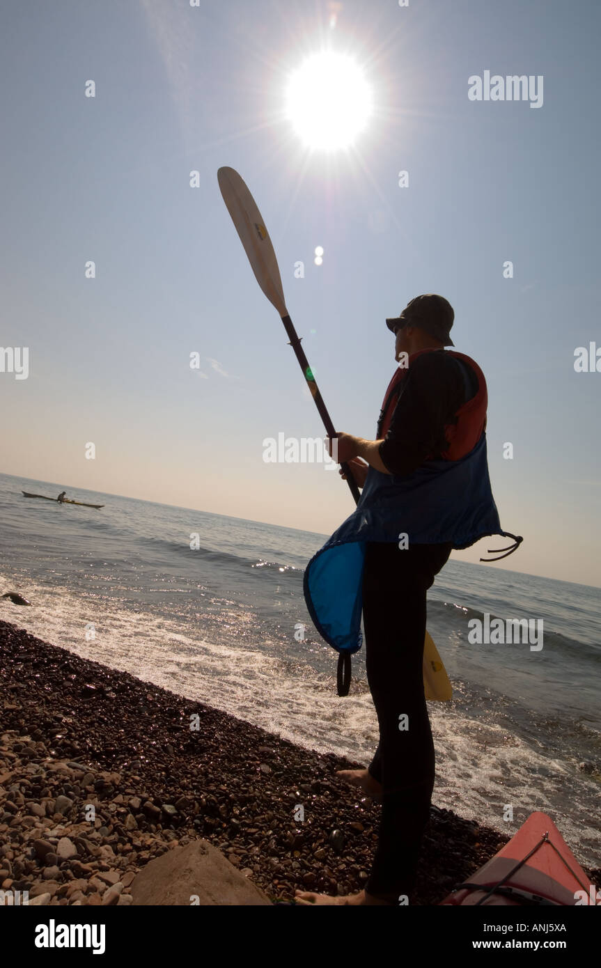 BACKLIT KAYAKER WITH PADDLE LOOKING AT A KAYAK IN LAKE SUPERIOR ON MINNESOTA'S NORTH SHORE Stock Photo