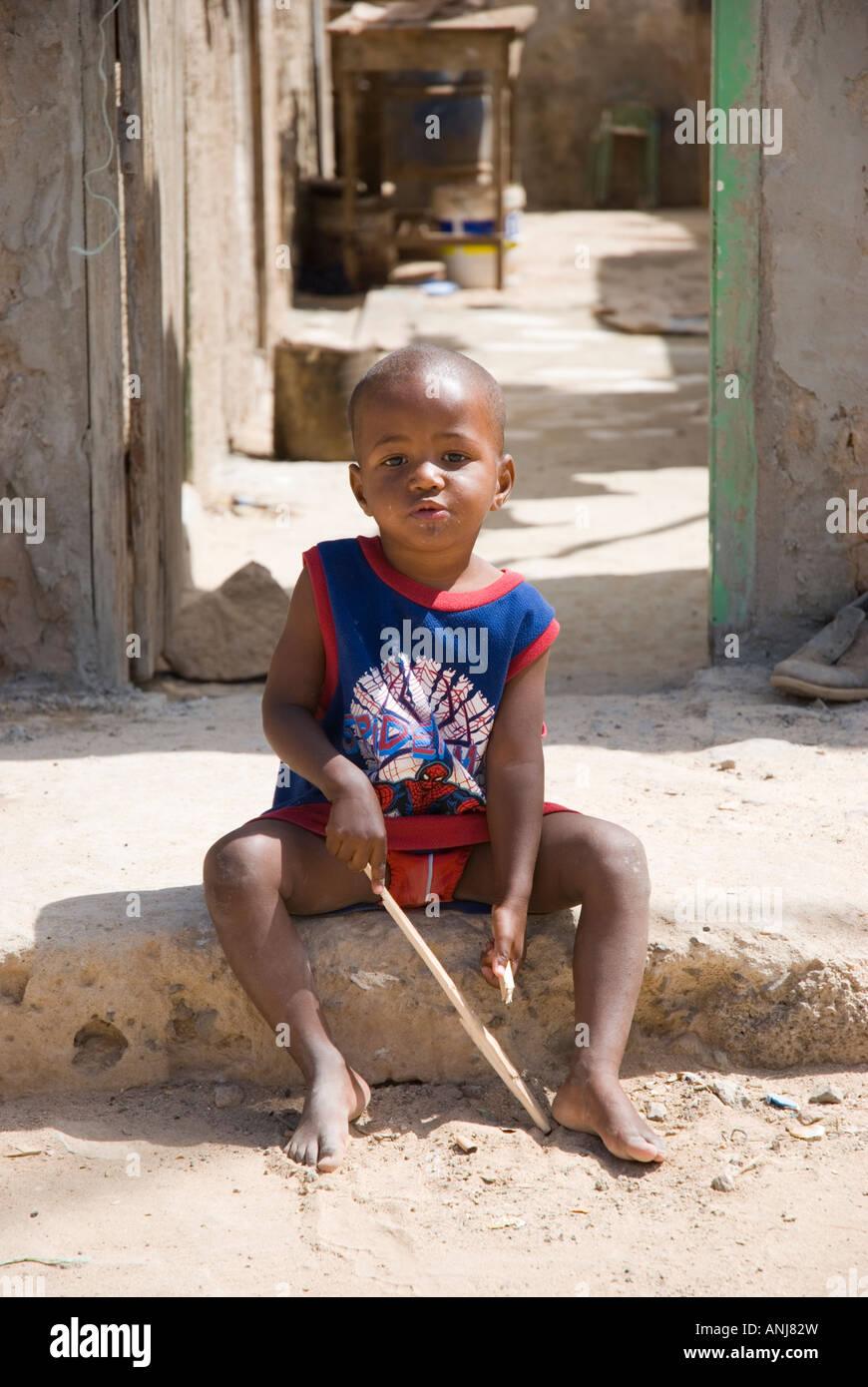 A colour portrait of a young boy sat on the roadside in a poor area of Santa Maria in the Cape Verde islands. Stock Photo