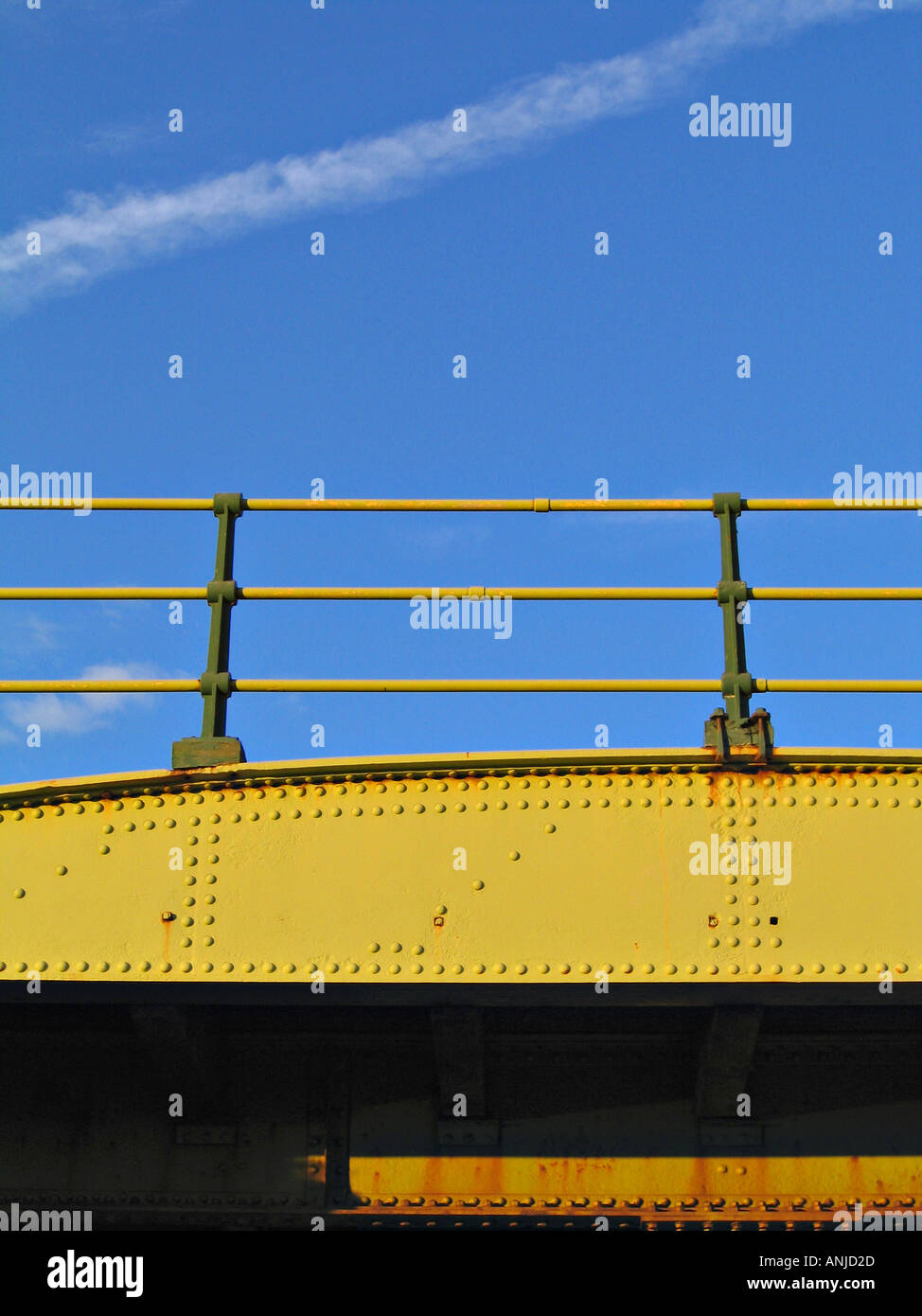Old, riveted railway bridge lit by evening sun with a blue sky behind. Stock Photo